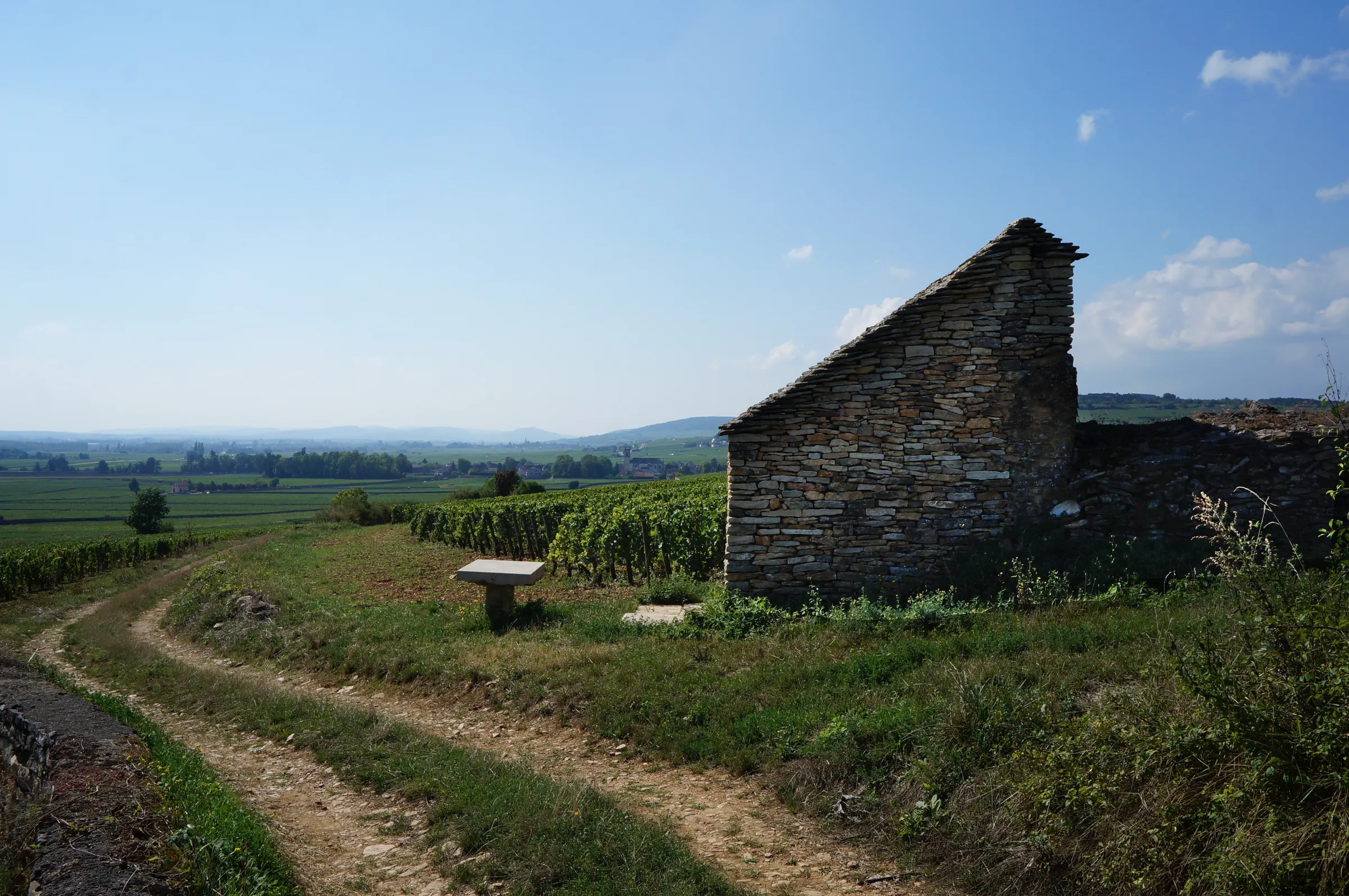 Dry-stone vineyard hut beside a dirt track overlooking vines and the valley near Beaune