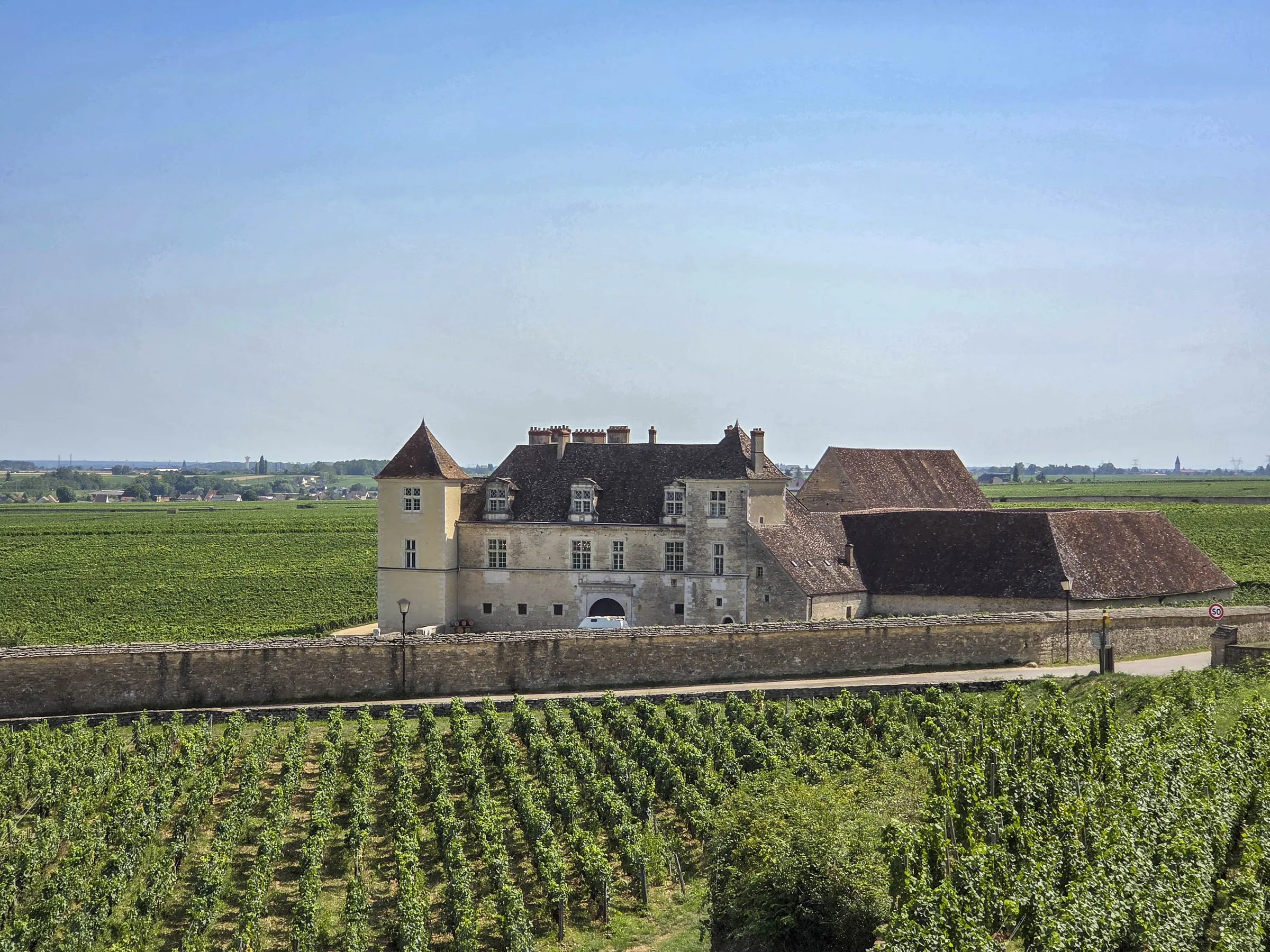 Château du Clos de Vougeot behind its stone wall, surrounded by green vineyard rows under a clear blue sky