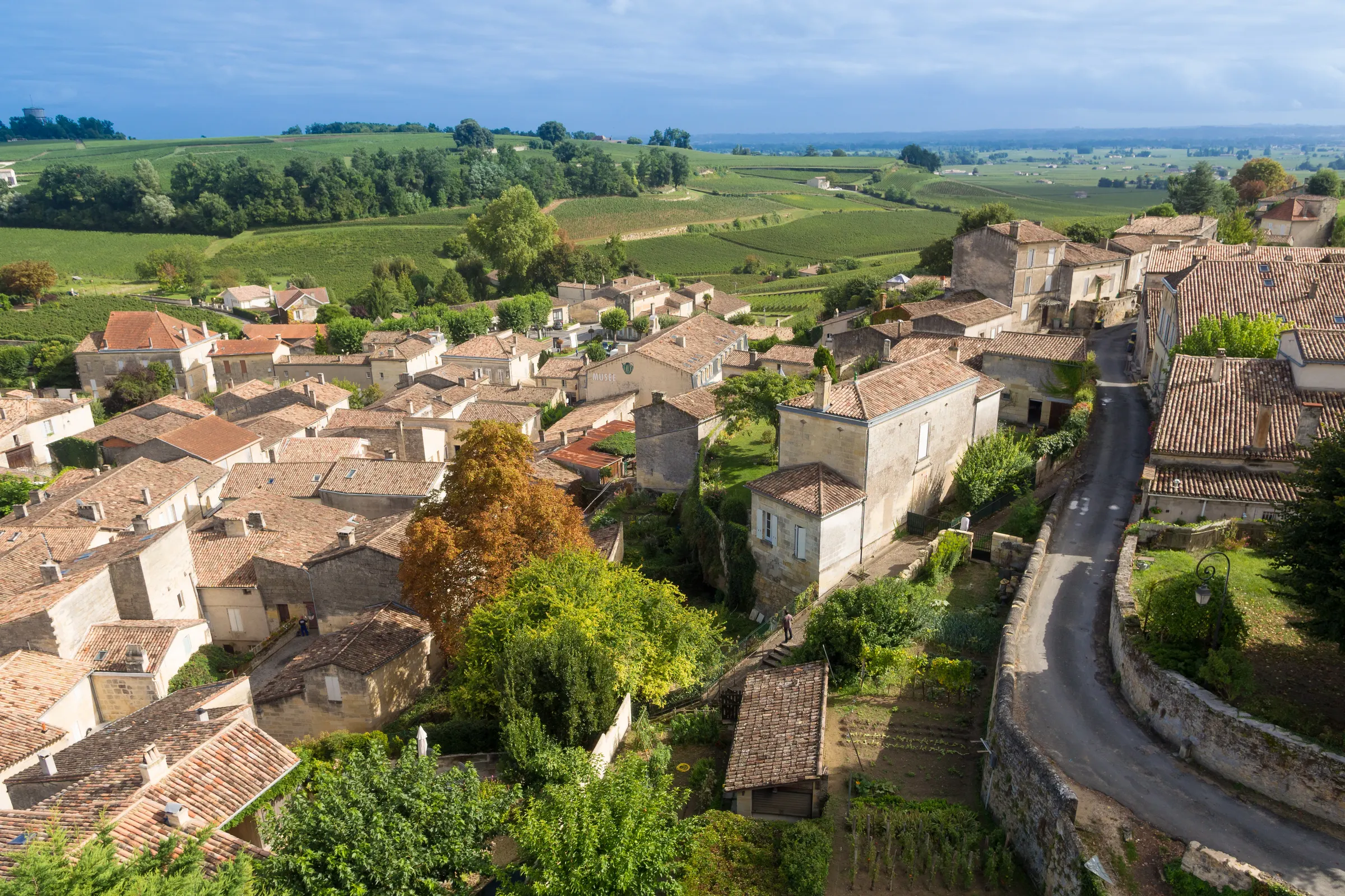 Aerial view over Saint-Émilion stone houses and a quiet road toward rolling green vineyards